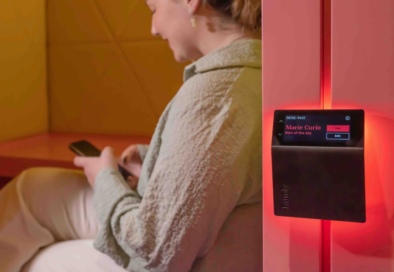 Rumsbokningspanel som lyser rött, kvinna sitter i bakgrunden